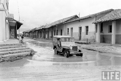         Niño mirando un jeep cruzar el charco de agua formado en la calle Pari esquina Independencia – fotografía 2 de 3
